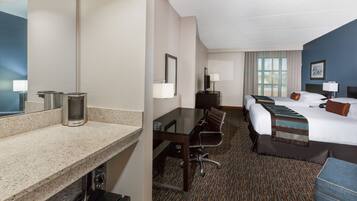 A hotel room with a bed, a desk with chairs, a large mirror, and a window with curtains.