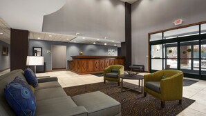 En lobby med reception, sofa, to lænestole, sofabord og et mønstret tæppe.
