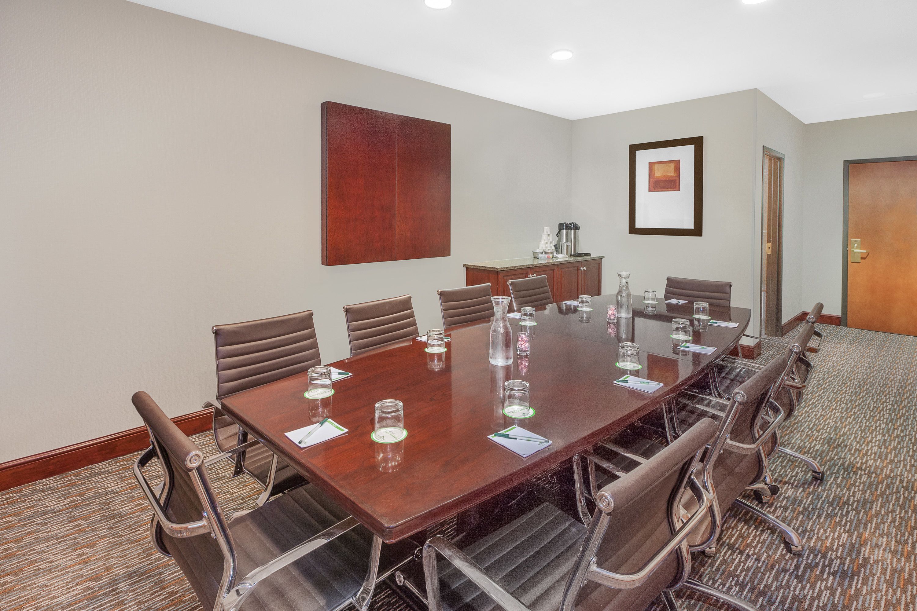 A conference room with a large wooden table, brown leather chairs, and a carpeted floor.