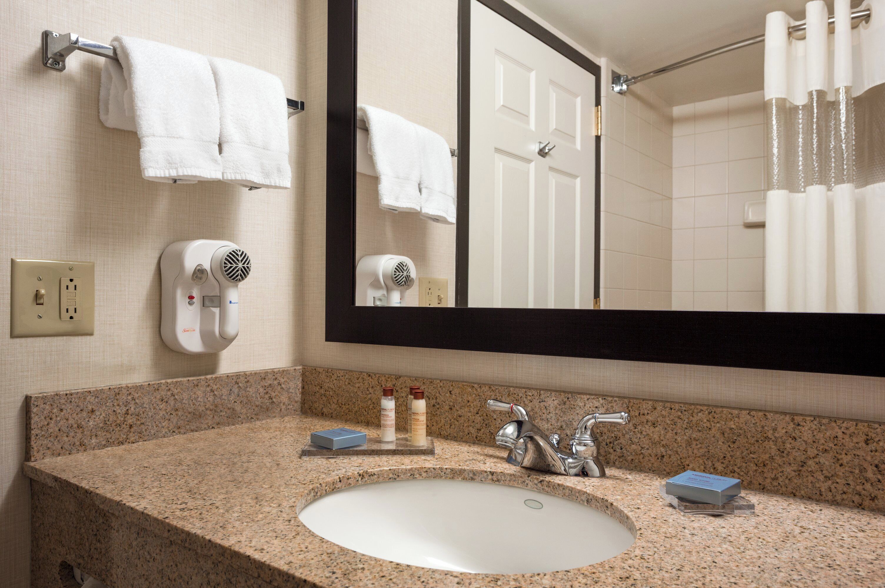 Un baño con encimera de granito, un lavabo blanco, un espejo y dos toalleros con toallas blancas.