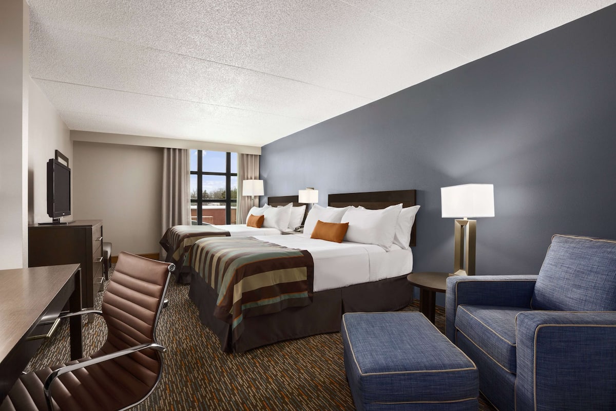 A hotel room with a large bed, two smaller beds, a desk, a chair, and a couch.