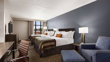 A hotel room with a large bed, two smaller beds, a desk, a chair, and a couch.