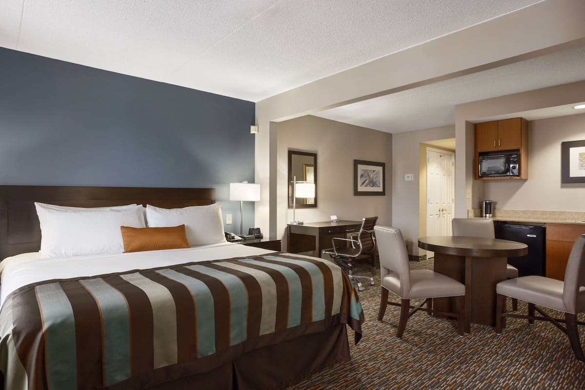 A hotel room with a large bed, a desk, two chairs, a microwave, and a coffee machine.
