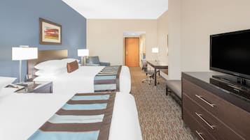 Habitación de hotel con dos camas, un escritorio, un televisor y una puerta al baño.