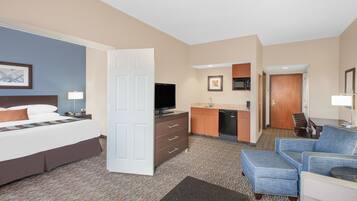 A hotel room with a bed, a desk, a kitchenette, and a seating area.