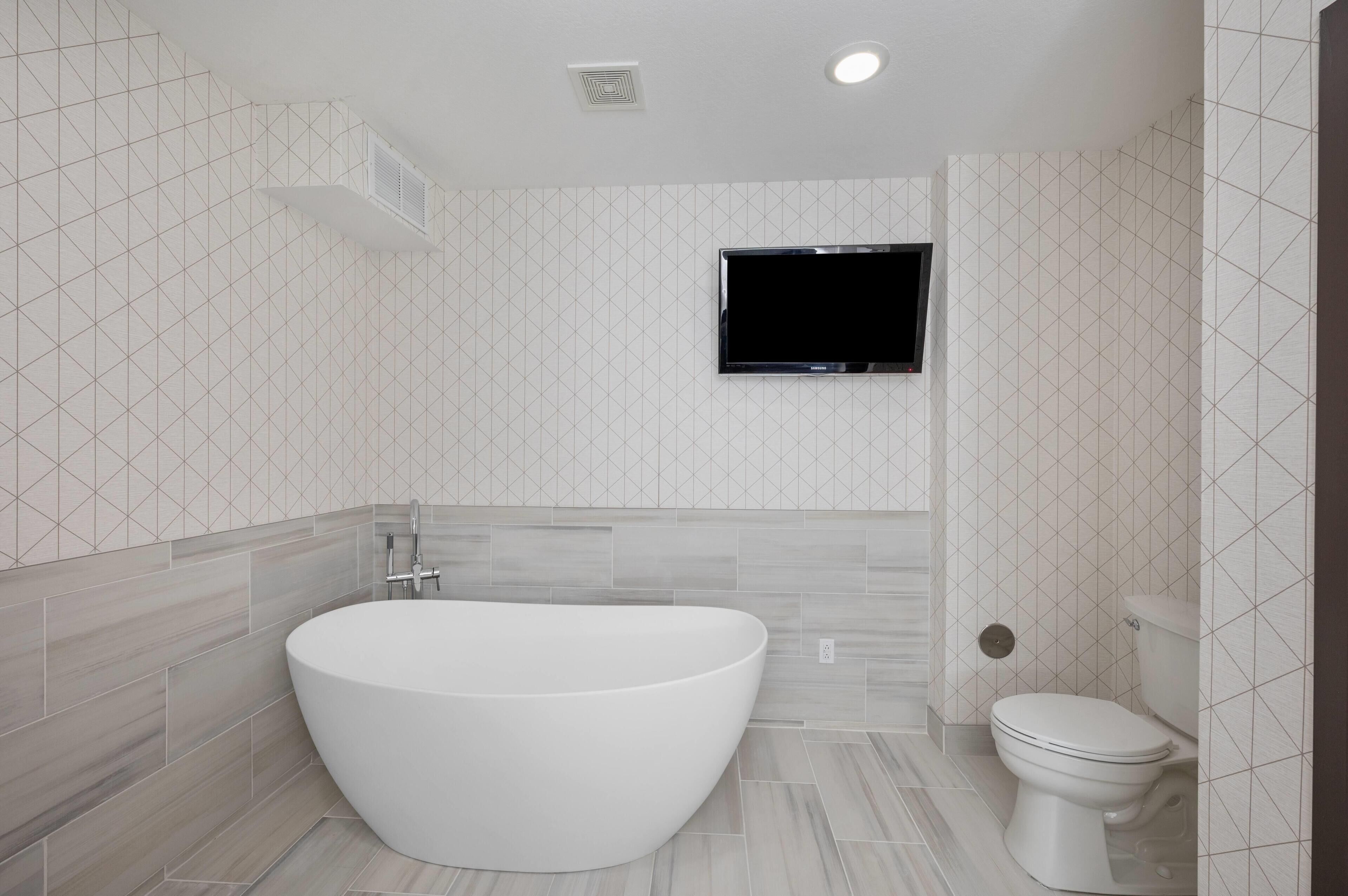 A modern bathroom with a freestanding bathtub, a toilet, and a wall-mounted TV.