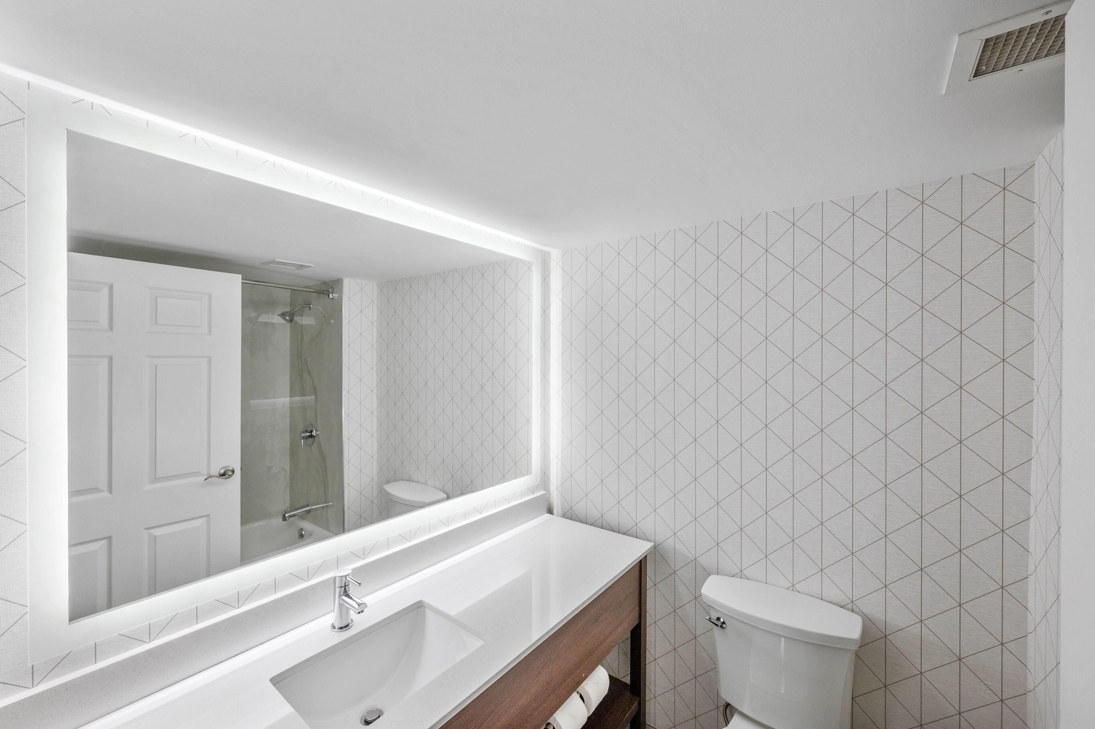 Et badeværelse med hvid vask, spejl og toilet.