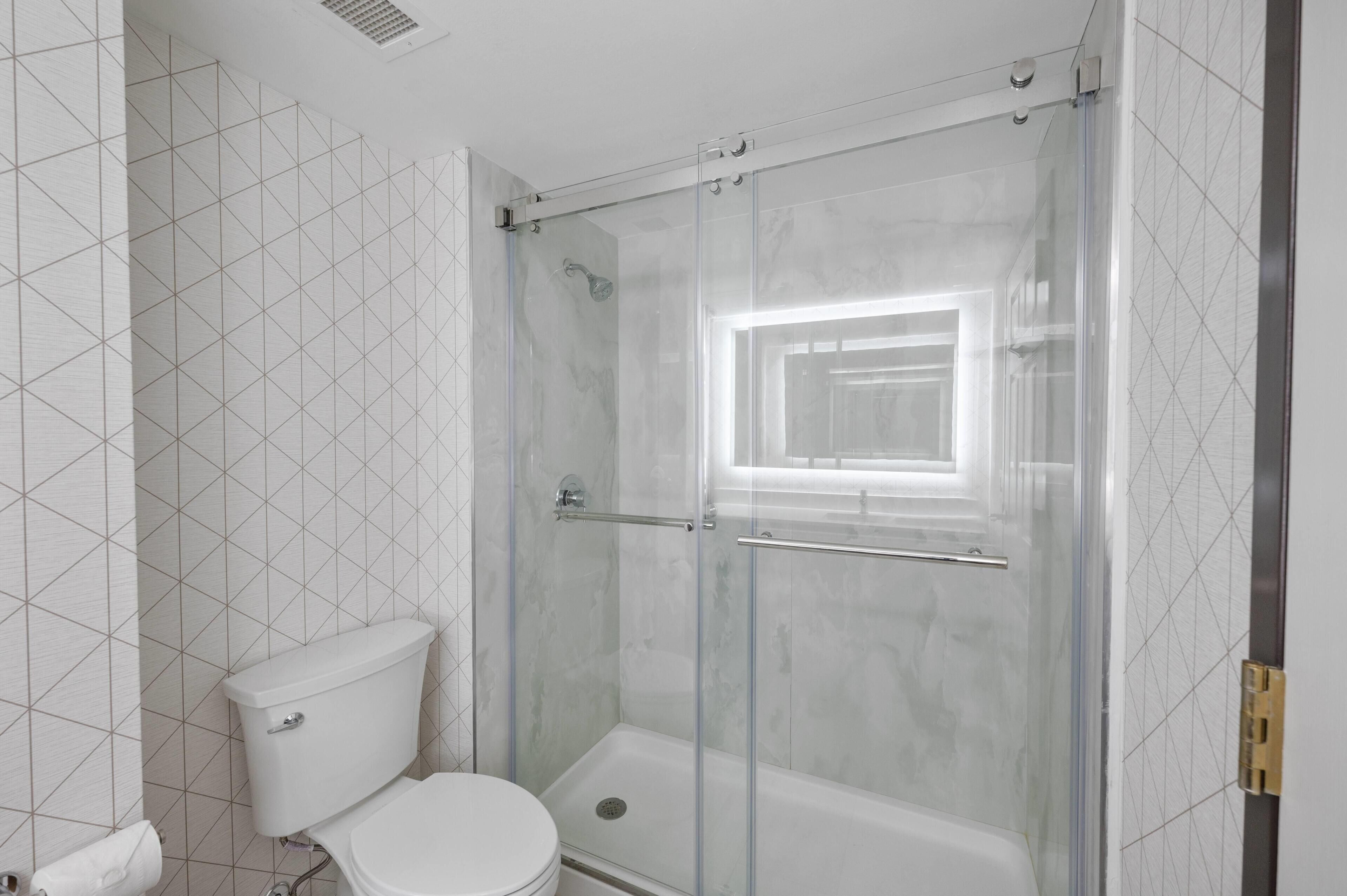 Un baño con inodoro, ducha con puerta de cristal y ventana.
