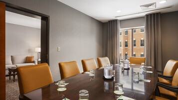 A conference room with a large table, leather chairs, and a view of a brick building through large windows.