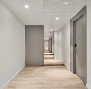 A modern hallway with a wooden floor, white walls, and a series of doors leading to rooms. - Hostal Lami (Esplugues de Llobregat)