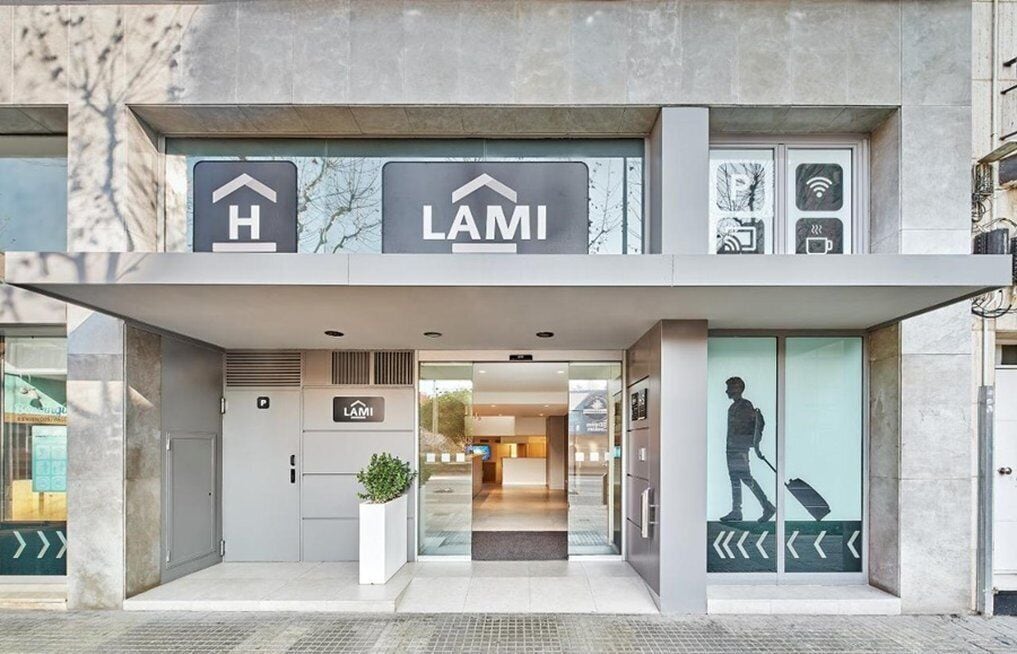 Een moderne hotelentree met een receptiebalie, een bord met daarop de naam van het hotel en een digitaal scherm.