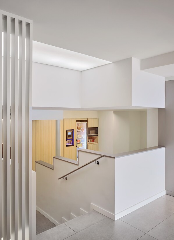 A modern interior with a staircase leading to a lower level, a built-in kitchen area, and a vending machine. - Hostal Lami (Esplugues de Llobregat)