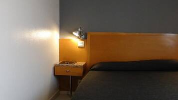 Una habitación de hotel con cabecera de madera, una mesita de noche con lámpara y una cama de color oscuro.