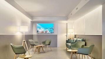 A modern hotel room with a seating area, a television, and a large window.