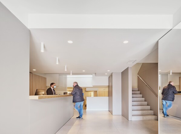 A modern hotel lobby with a reception desk, a staircase, and a minimalist design. - Hostal Lami (Esplugues de Llobregat)