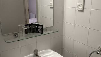 Un baño con un lavabo blanco, un estante de vidrio encima y una toalla colgada en un perchero.
