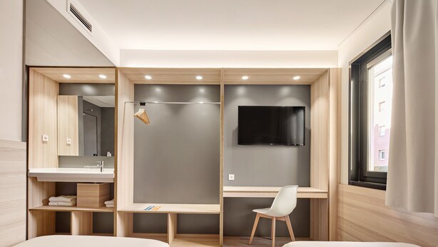 Een moderne hotelkamer met twee bedden, een bureau, een televisie en een raam met gordijnen.