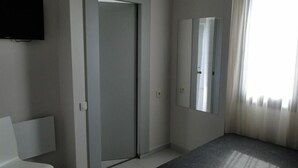Een hotelkamer met een gesloten deur, een grote spiegel en een raam met gordijnen.