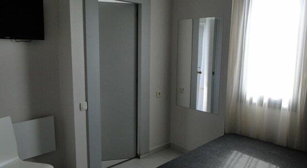 A hotel room with a closed door, a large mirror, and a window with curtains. - Hostal Lami (Esplugues de Llobregat)