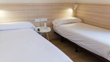A twin room with two single beds, a small bedside table with a lamp, and a wall-mounted power outlet.