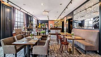 A restaurant with a mix of booths and tables, a brick floor, and a bar area visible through a glass partition.