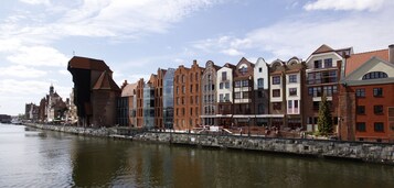 A riverside promenade with historic buildings, a stone wall, and a clear sky.