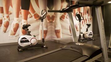 A gym with treadmills and stationary bikes, featuring a large mirror and a wall with a ballet dancer's reflection.