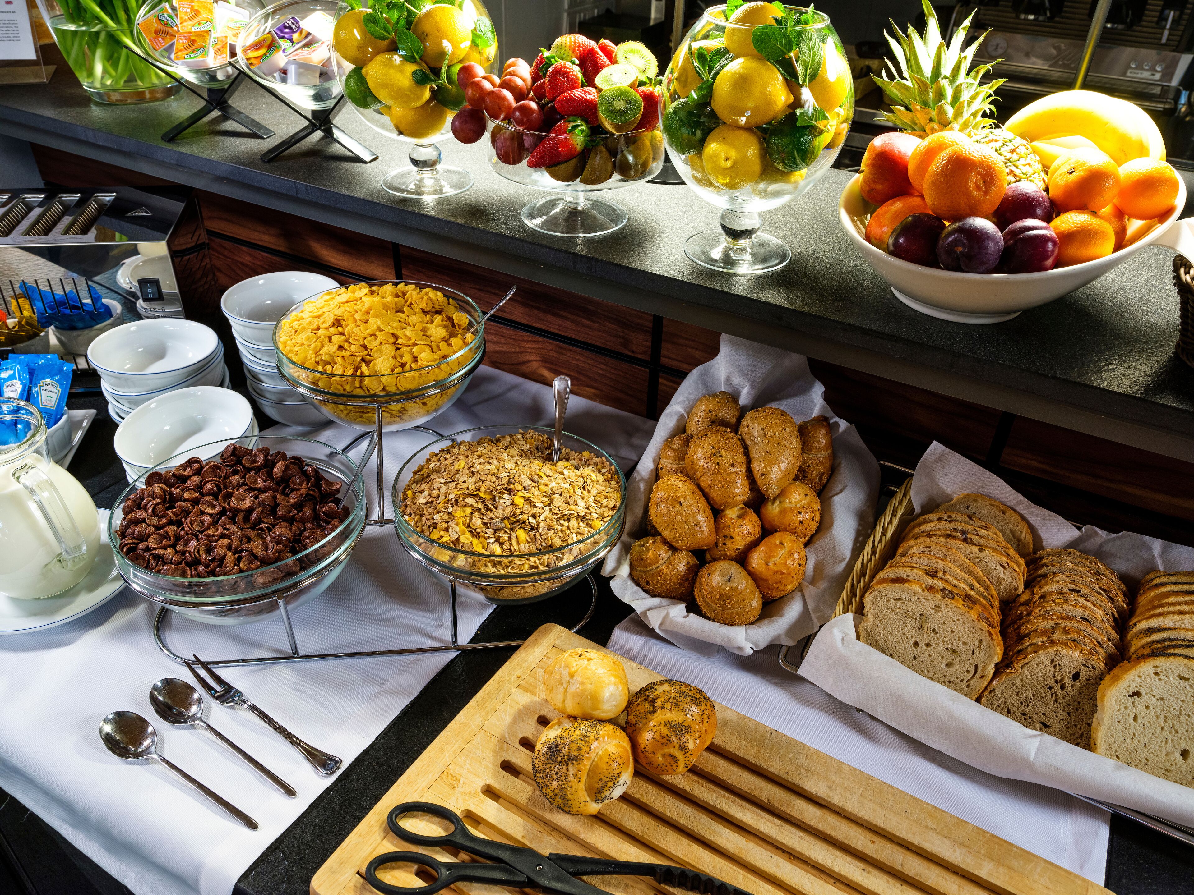 Un bufé con diversos alimentos, entre ellos frutas, cereales y pan.