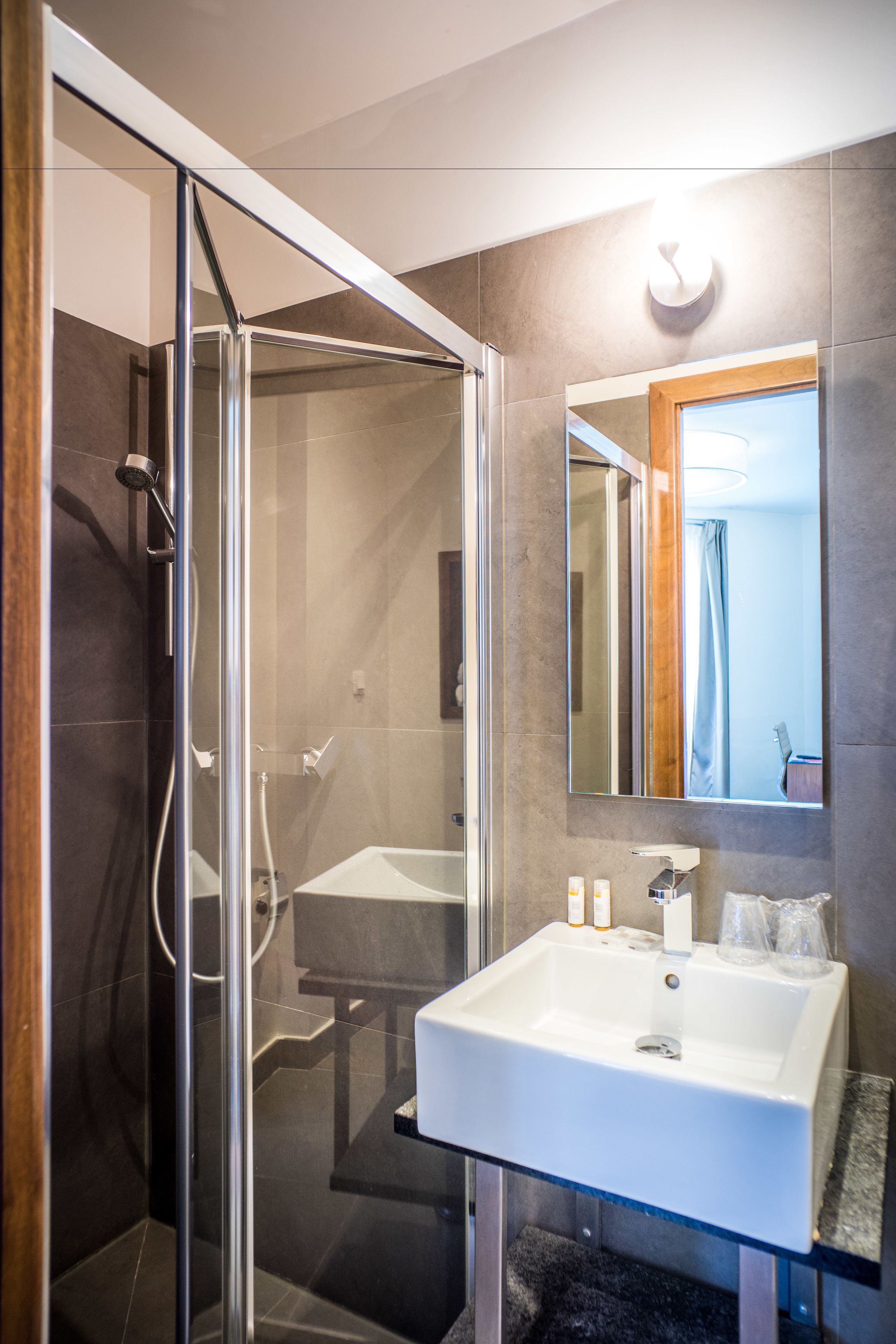 A modern bathroom with a glass-enclosed shower, a white sink, and a mirror with a wooden frame.