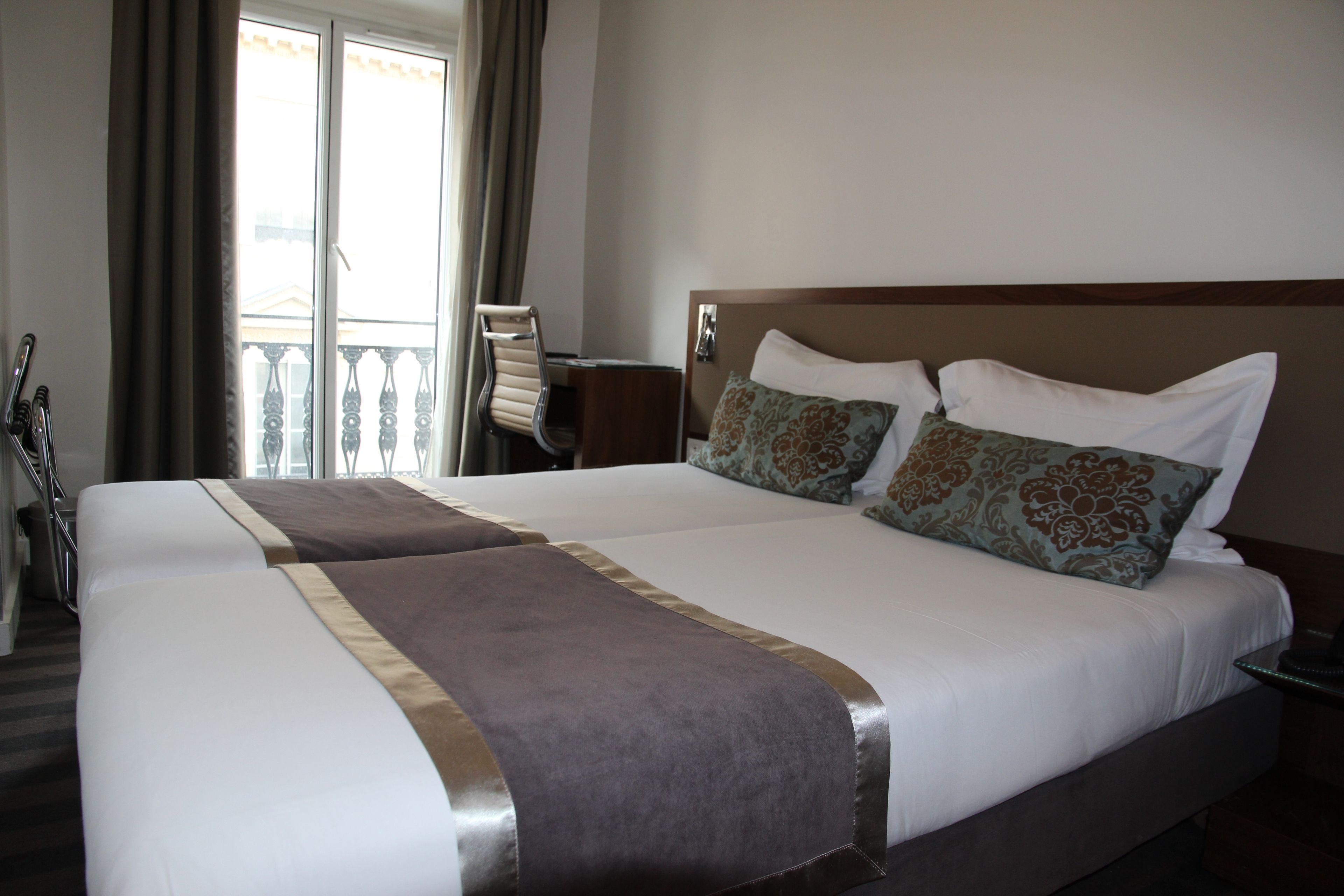 A hotel room with two beds, a balcony, and a chair.