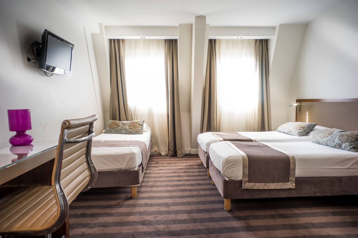 A hotel room with two beds, a desk, a chair, a TV, and curtains.