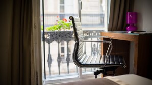 A hotel room with a view of a balcony, a chair, a wooden desk, and a purple lamp. - Art Hotel (Paris)