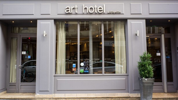 The exterior of an art hotel with a classic facade, large windows, and a small planter in front. - Art Hotel (Paris)