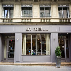 The exterior of an art hotel with a classic facade, large windows, and a small planter in front. - Art Hotel (Paris)