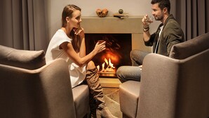 A couple seated on a couch facing a fireplace with a book and decorative items on the mantel.