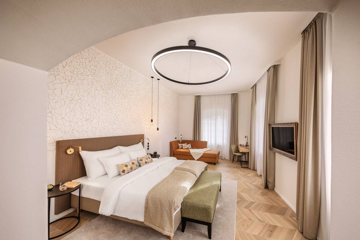 A modern hotel room with a large bed, a sofa, a TV, and a circular ceiling light.