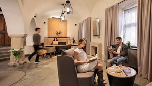 A modern hotel lobby with a seating area, a dining space, and a reception desk.