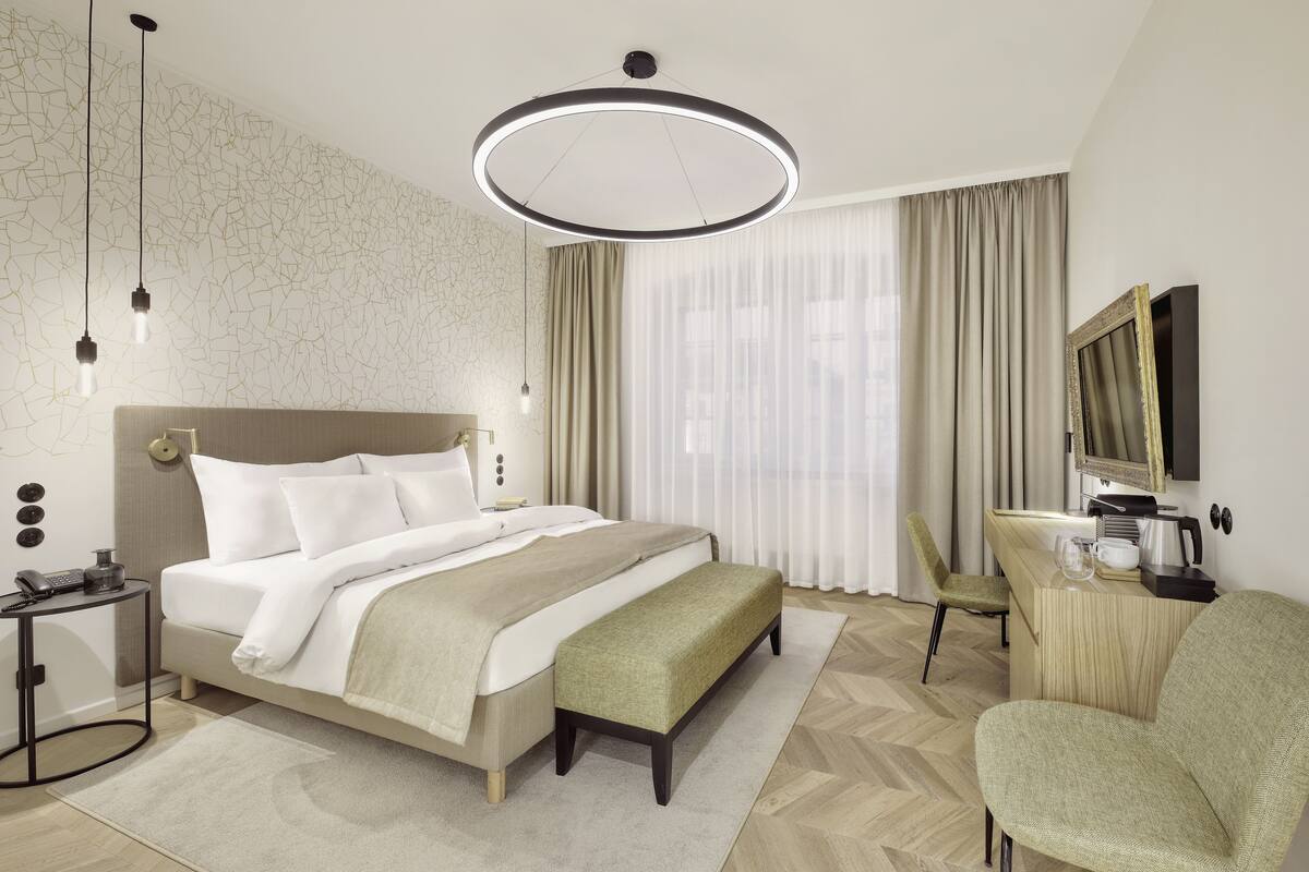 A modern hotel room with a large bed, a desk, a chair, and a television.