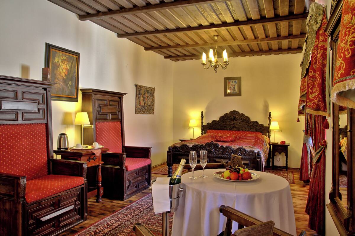 A traditional room with a wooden bed, a small table with a fruit plate, and a bottle of champagne.