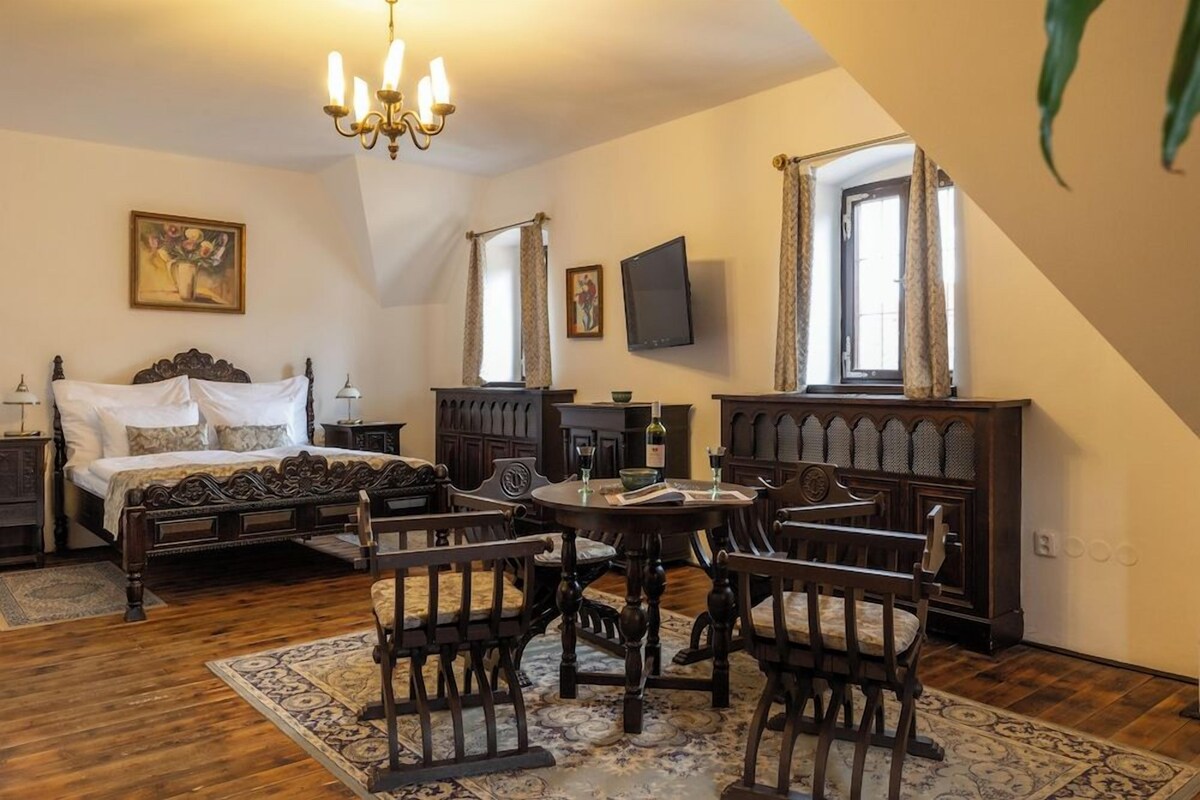 Un dormitorio con cama, una araña, televisor y comedor con sillas y mesa.