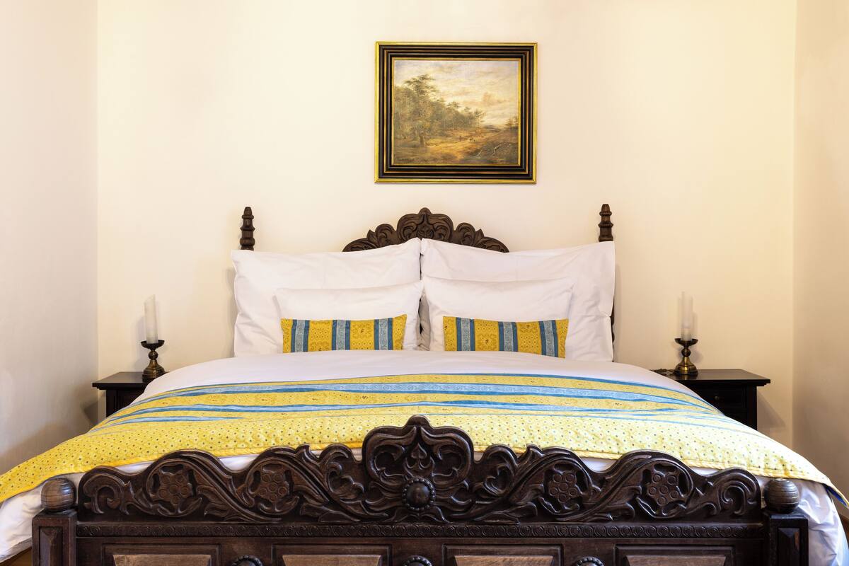 A neatly made bed with a patterned bedspread, a wooden headboard, and two bedside tables with candles.