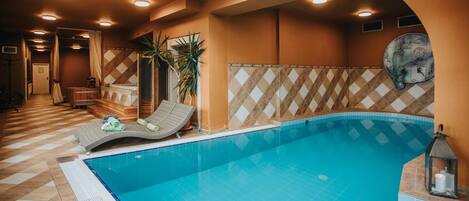 Ein Hallenbad mit gefliestem Boden, Liegestühlen und einer Decke mit Einbautenbeleuchtung.