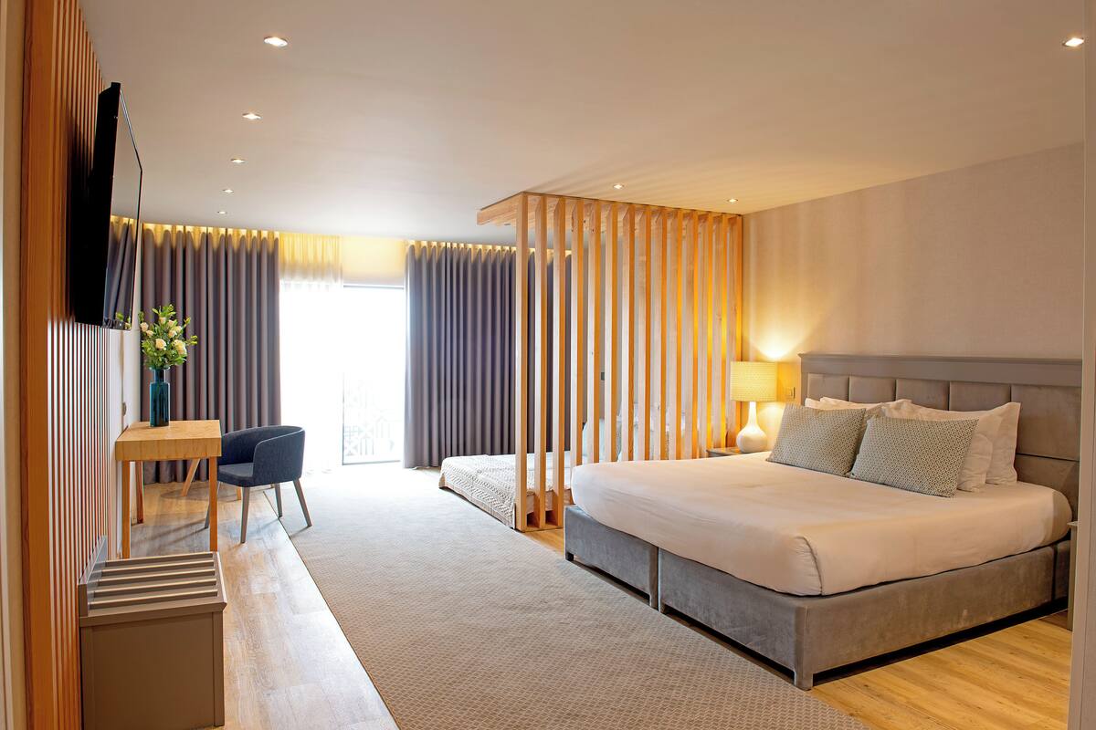 Ein modernes Hotelzimmer mit einem großen Bett, einem Schreibtisch, einem Sessel und einem an der Wand montierten Fernseher.