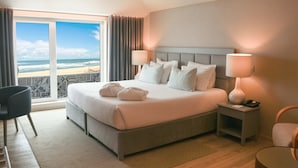 A hotel room with a large bed, two bedside tables, a chair, and a view of the beach.