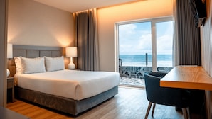 A hotel room with a large bed, a desk, and a view of the ocean.