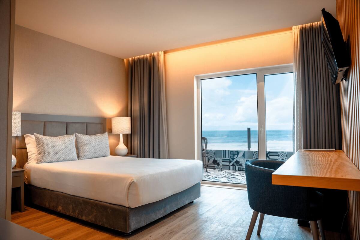 Ein Hotelzimmer mit einem großen Bett, einem Schreibtisch und Blick auf das Meer.