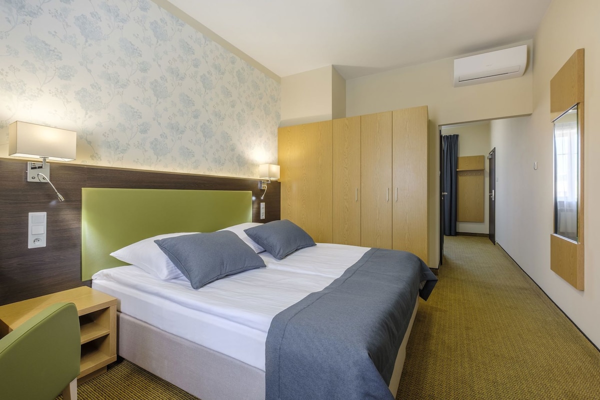 Una habitación de hotel con cama, mesita de noche, lámpara, armario y aire acondicionado.