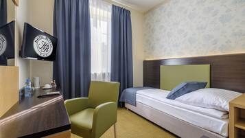 A hotel room with a bed, a desk with a television, a chair, and a window with curtains.