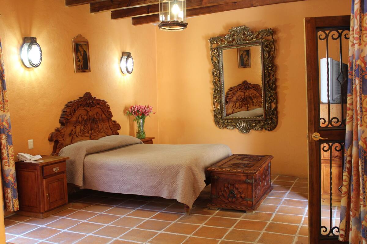 A bedroom with a wooden bed, a nightstand, a dresser, a mirror, and a door with a decorative iron gate.