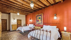Een kamer met twee bedden, houten balken in het plafond, een rode wand en een schilderij met fruit.